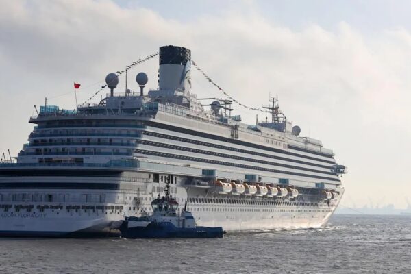 Adora Flora City viewed from the stern, with a tug alongside and the ship’s name visible on the hull.